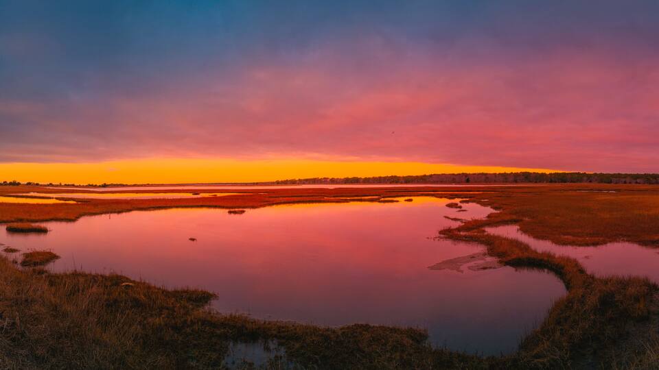 Sunrise panoramic seascape over the marsh pond in Mashpee on South Cape Beach, Massachusetts. Pink and blue western sky and water reflections at cloudy dawn.
