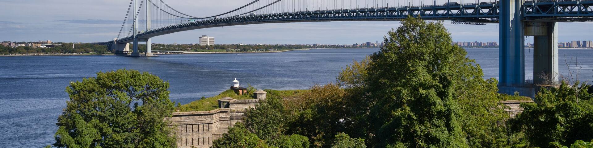 A large suspension bridge spanning a wide river, surrounded by lush greenery and a clear blue sky.