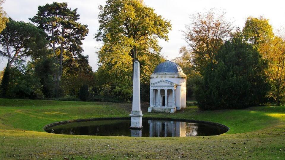 A gazebo with a dome roof surrounded by trees and a pond.