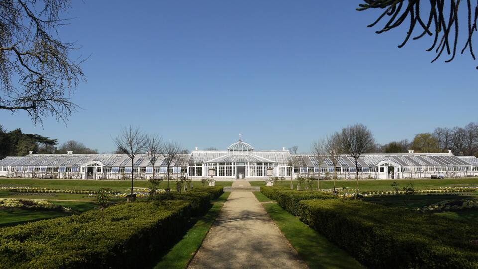 A large greenhouse with a dome roof, surrounded by manicured gardens and pathways.