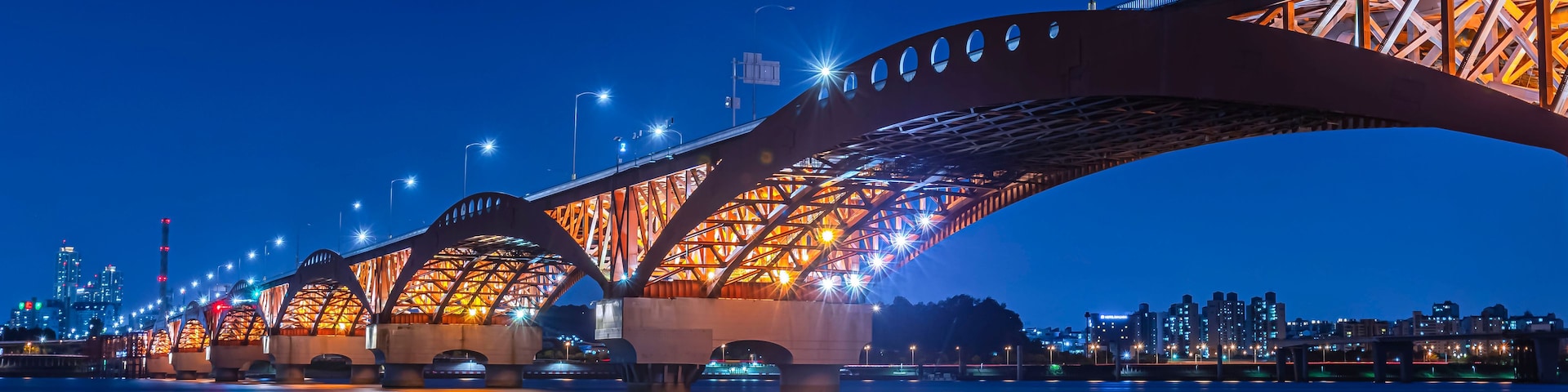 Uma ponte bem iluminada à noite, com seu reflexo na água.