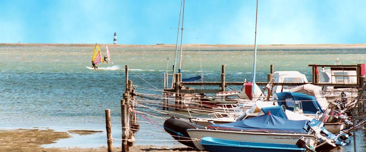 A beach with boats, a lighthouse, and a person windsurfing.