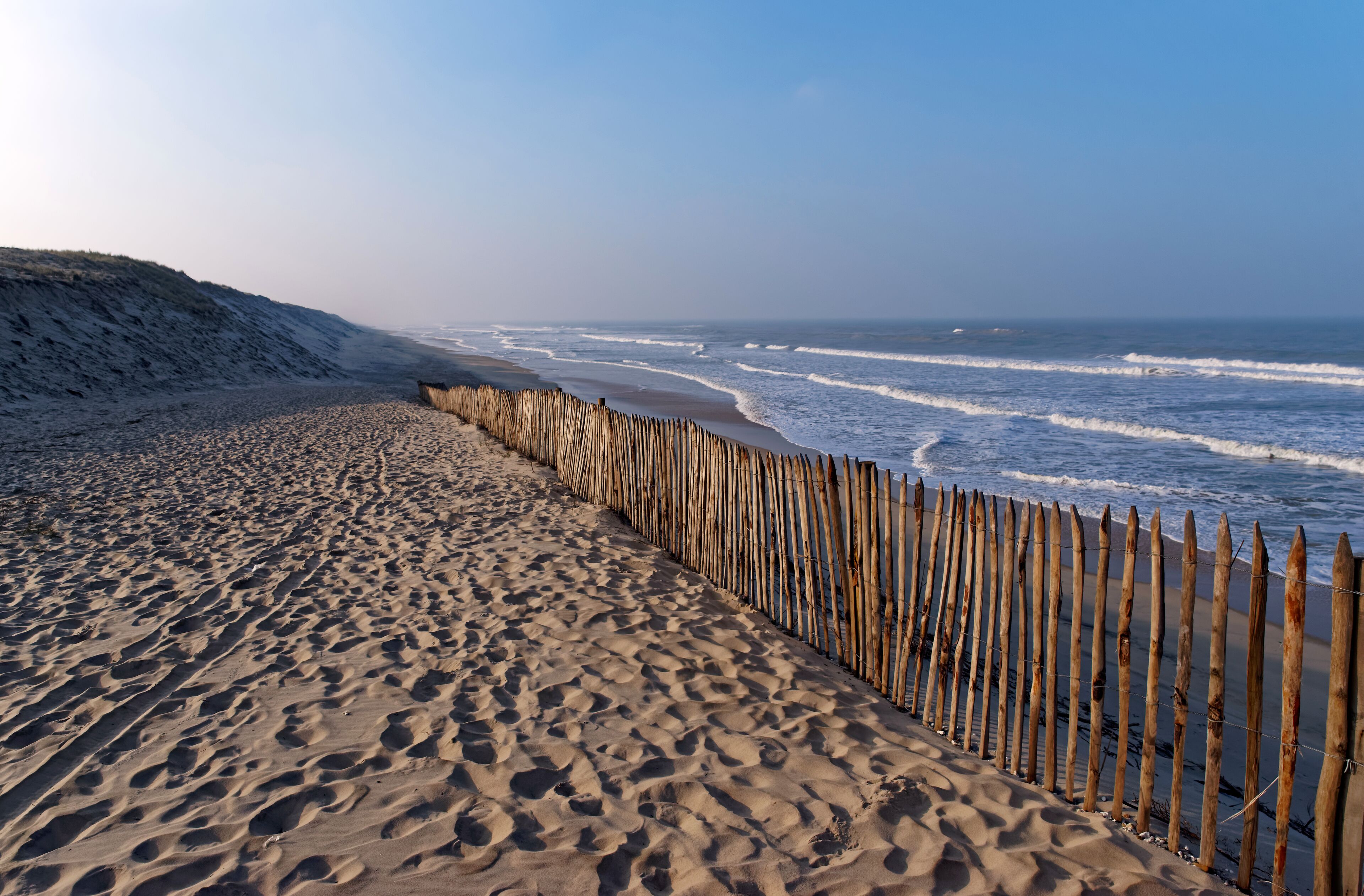 A sandy beach with a wooden fence and ocean waves.