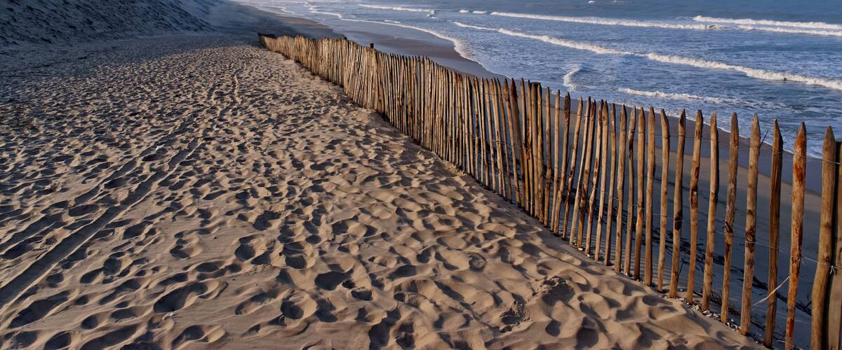 A sandy beach with a wooden fence and ocean waves.