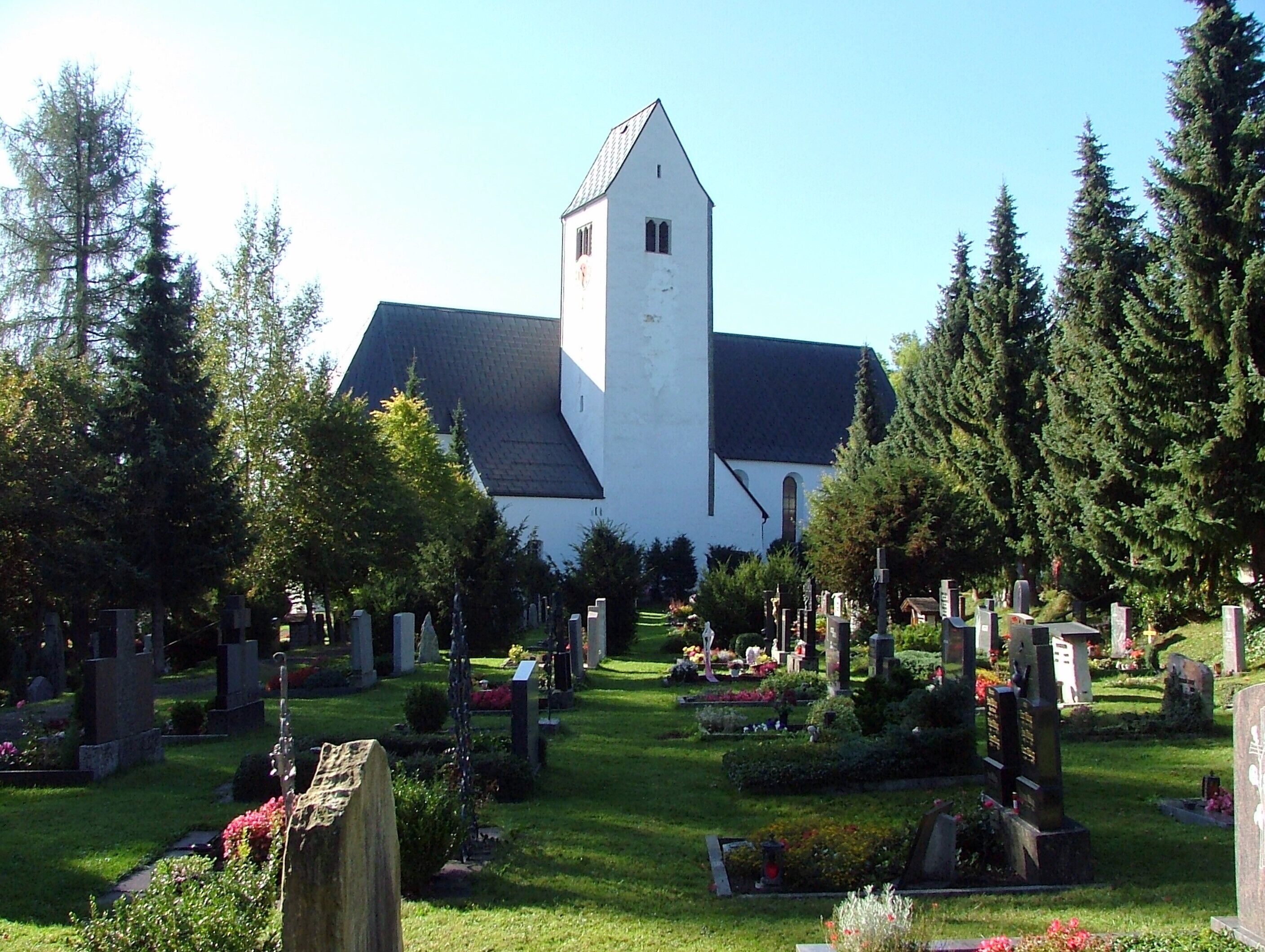 A church with a tall tower and a cemetery with gravestones and flowers.