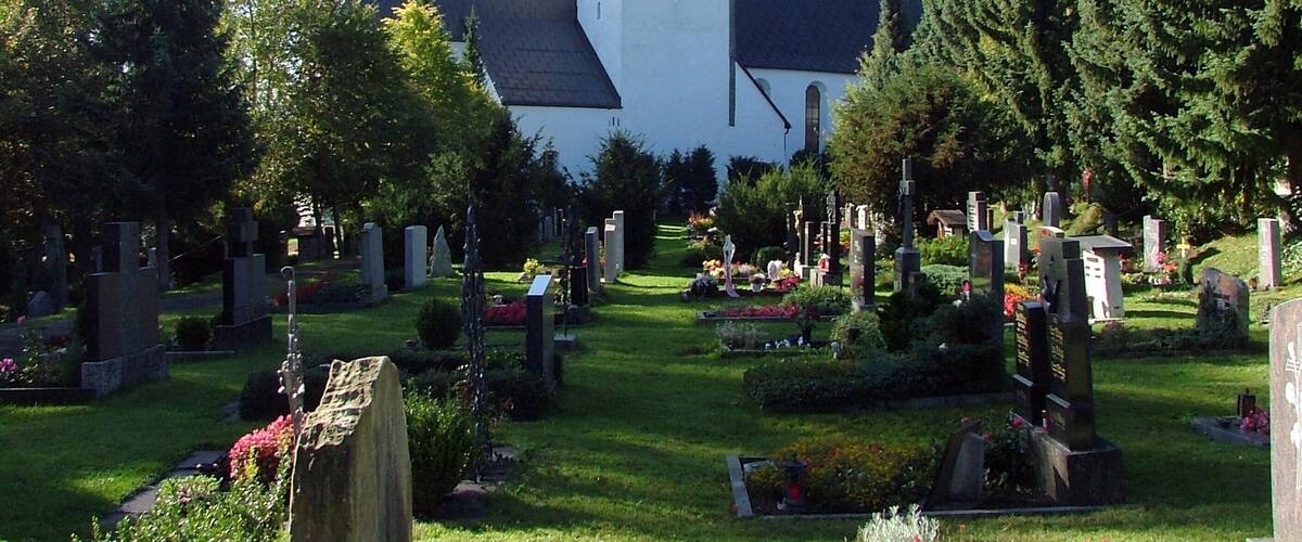A church with a tall tower and a cemetery with gravestones and flowers.
