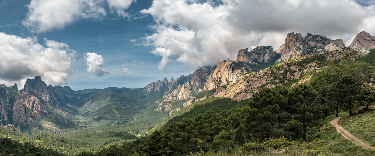 A mountainous landscape with rugged peaks and dense forest.