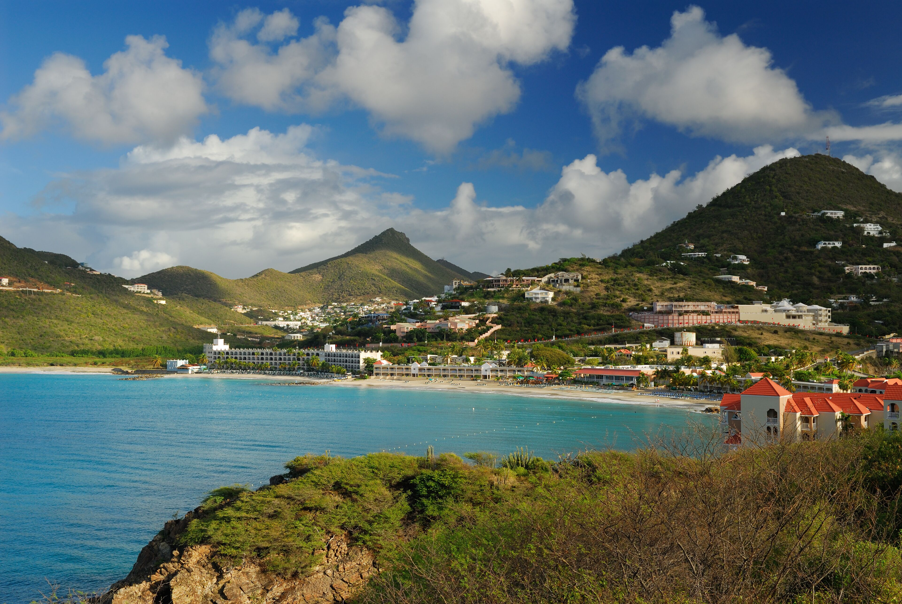 A coastal town with a beach, a mountain, and a clear blue sky.