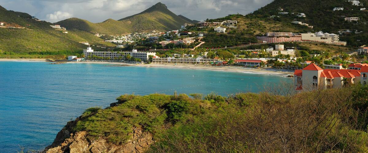 A coastal town with a beach, a mountain, and a clear blue sky.