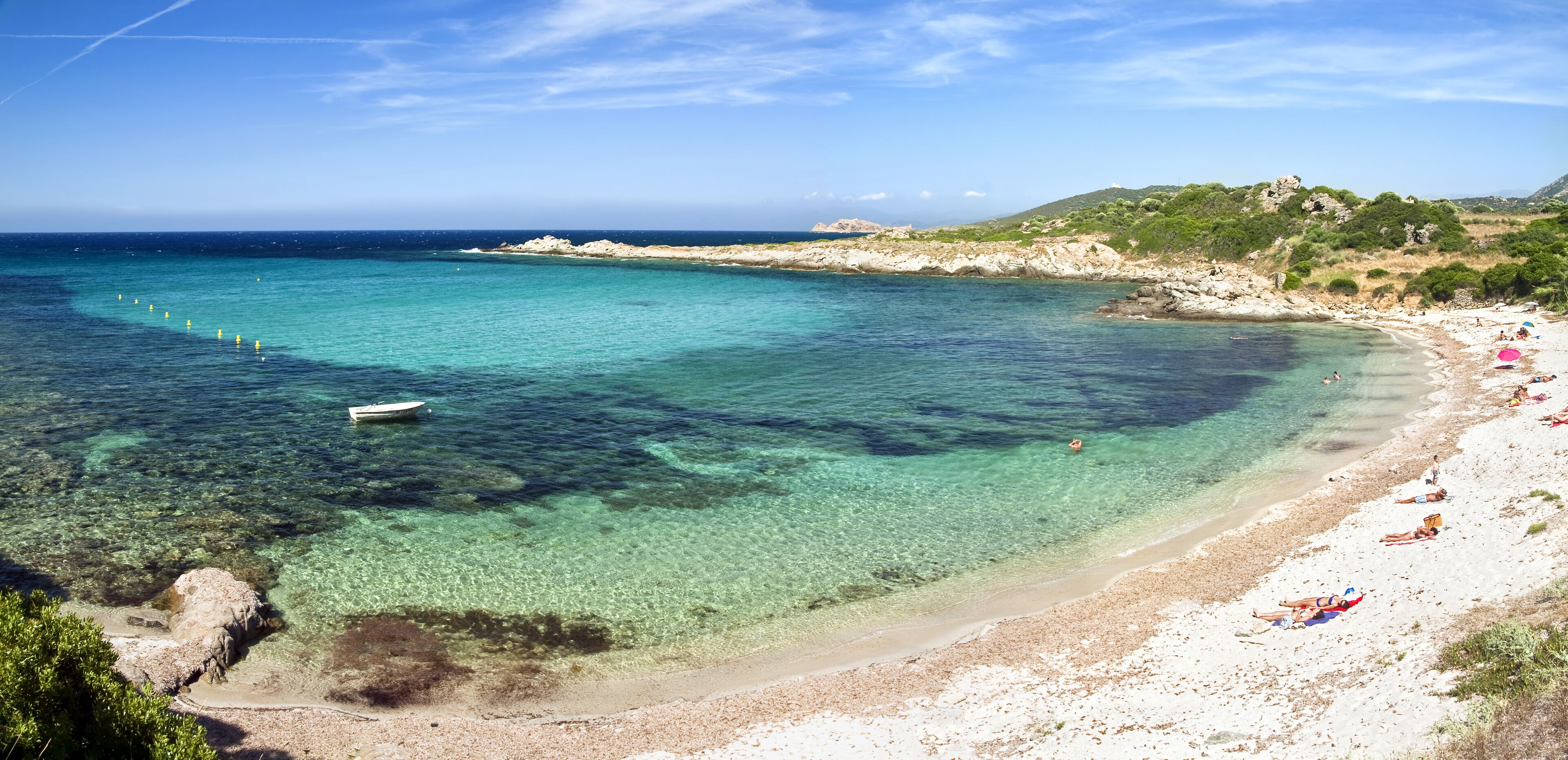 A clear turquoise sea, a sandy beach, and rocky hills in the background.