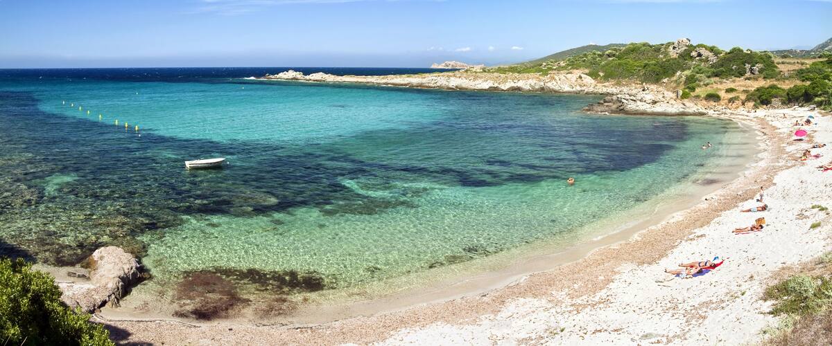 A clear turquoise sea, a sandy beach, and rocky hills in the background.