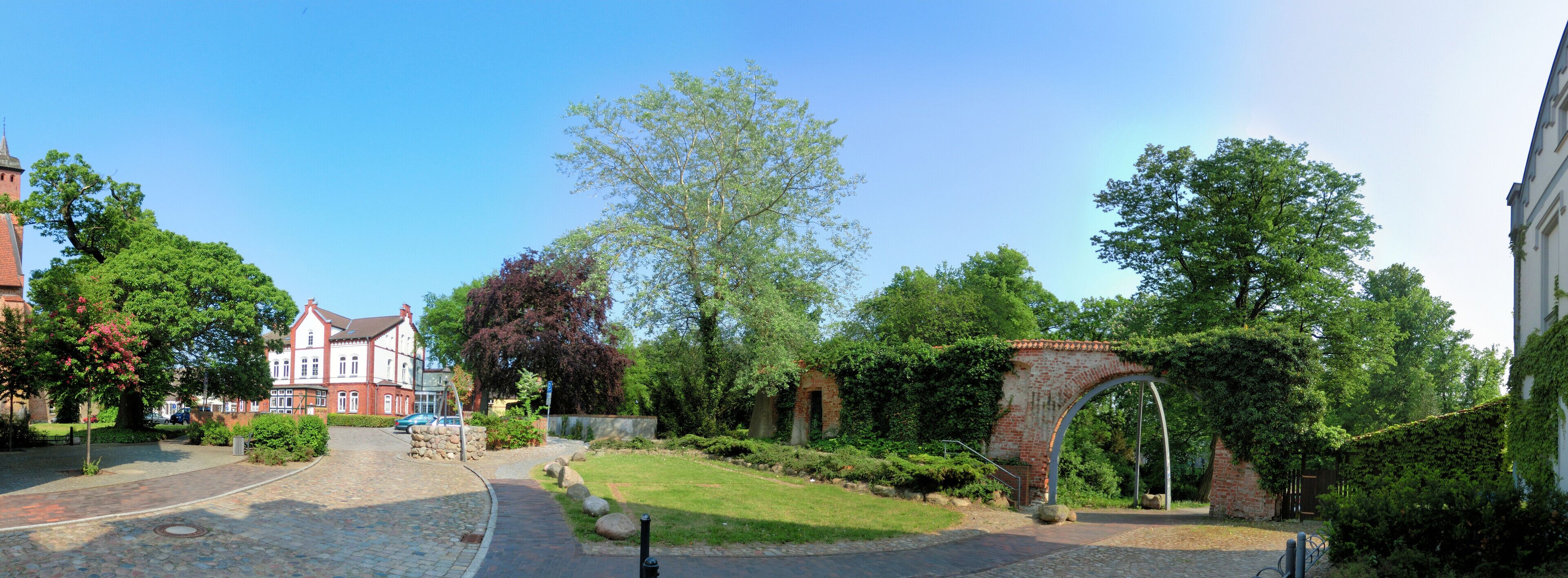 A cobblestone street with a brick archway, lush greenery, and historic buildings.