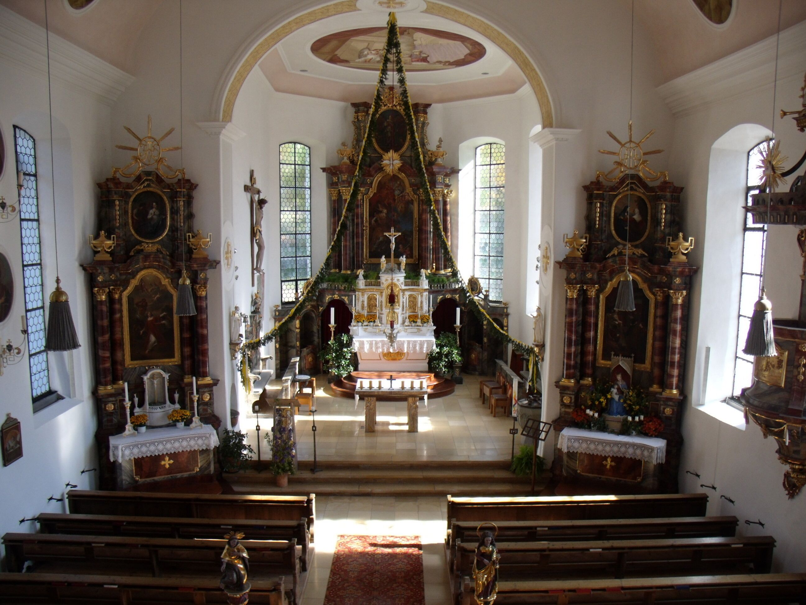 An ornate church interior with a central altar, pews, and stained glass windows.