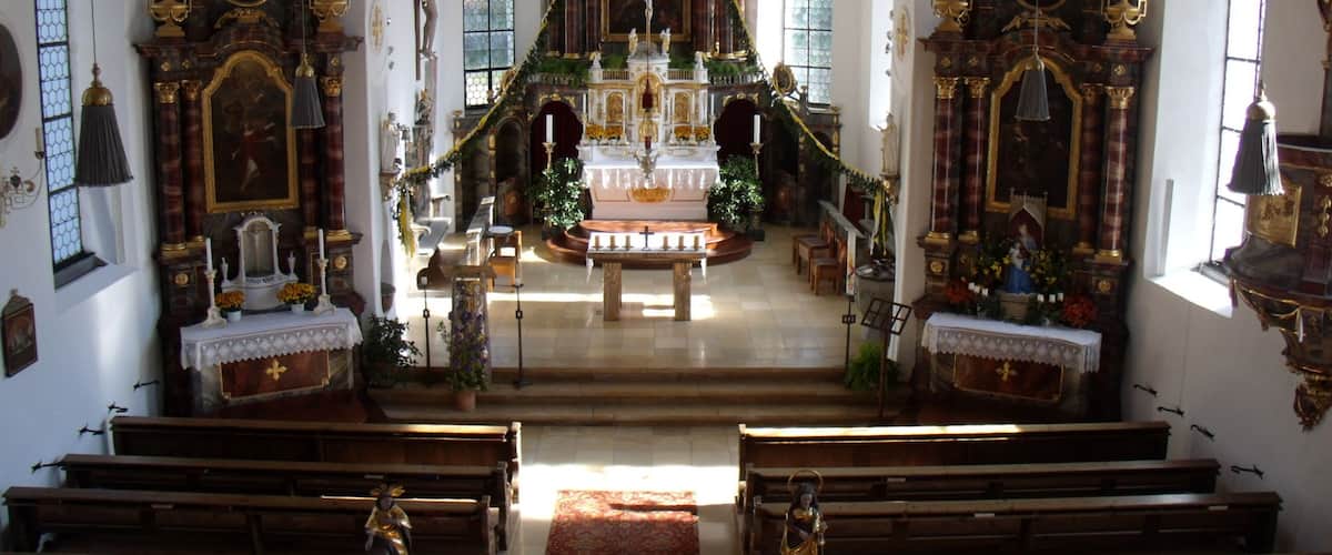 An ornate church interior with a central altar, pews, and stained glass windows.