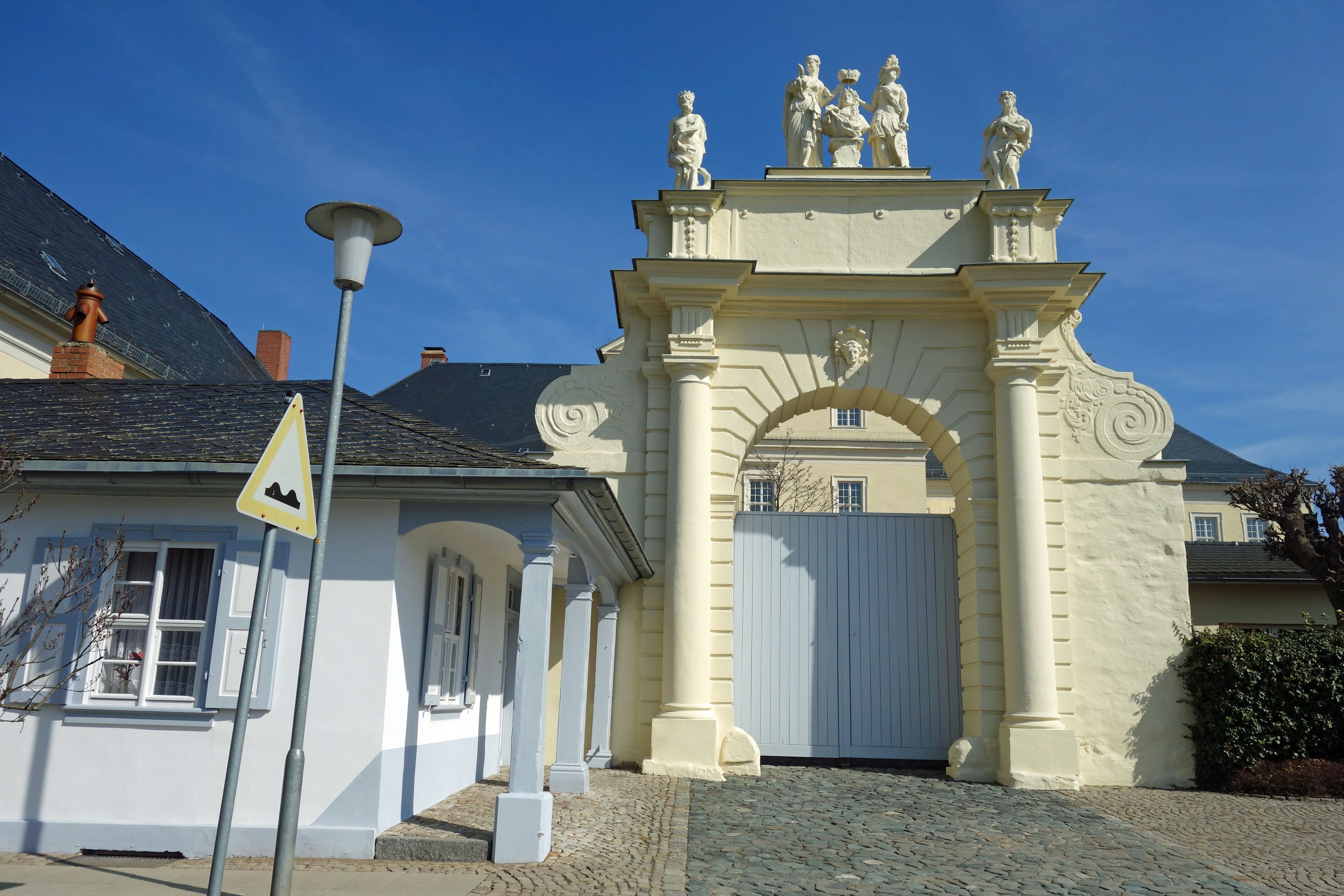 A classical building with a white facade, a stone entrance, and a statue atop.