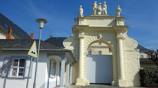 A classical building with a white facade, a stone entrance, and a statue atop.