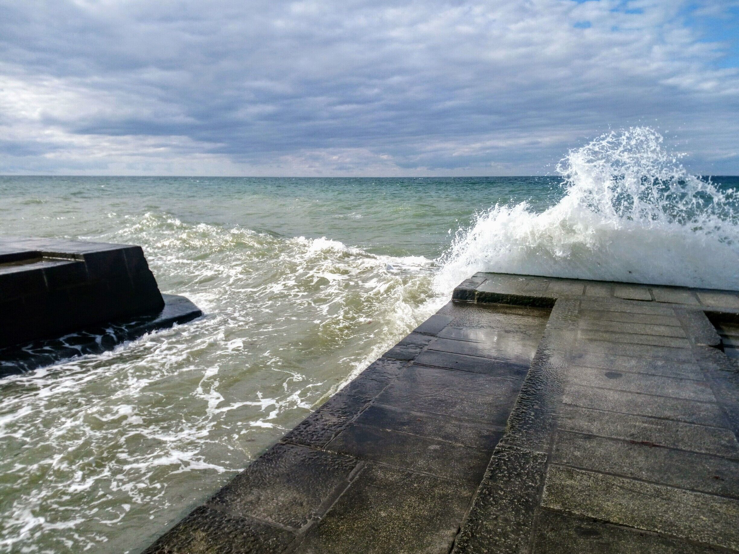A concrete pier with waves crashing against it.