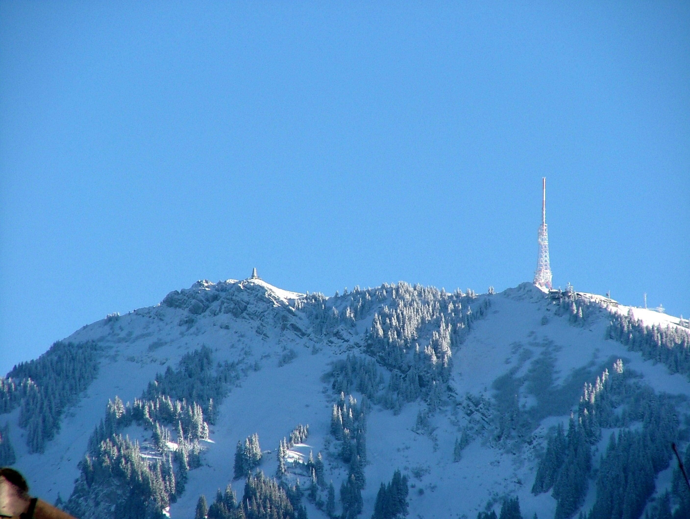 A snow-covered mountain with a tall radio tower on top.