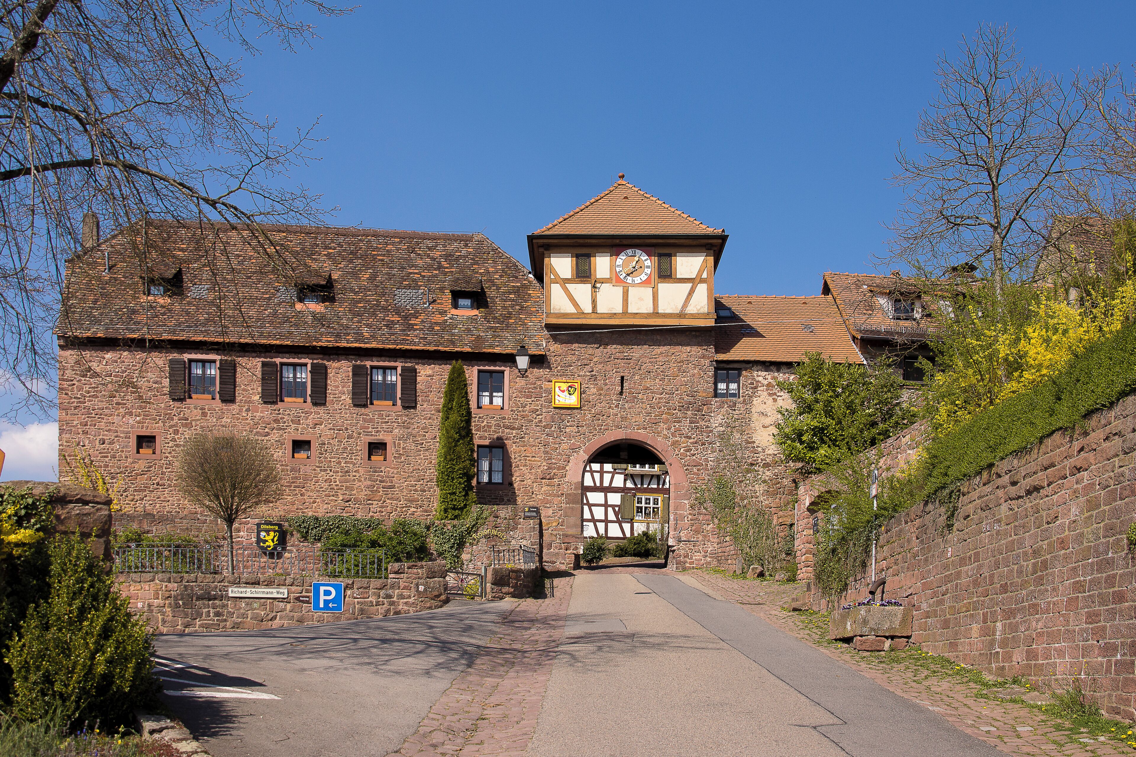 A historic stone building with a clock tower, a paved entrance, and a parking sign.