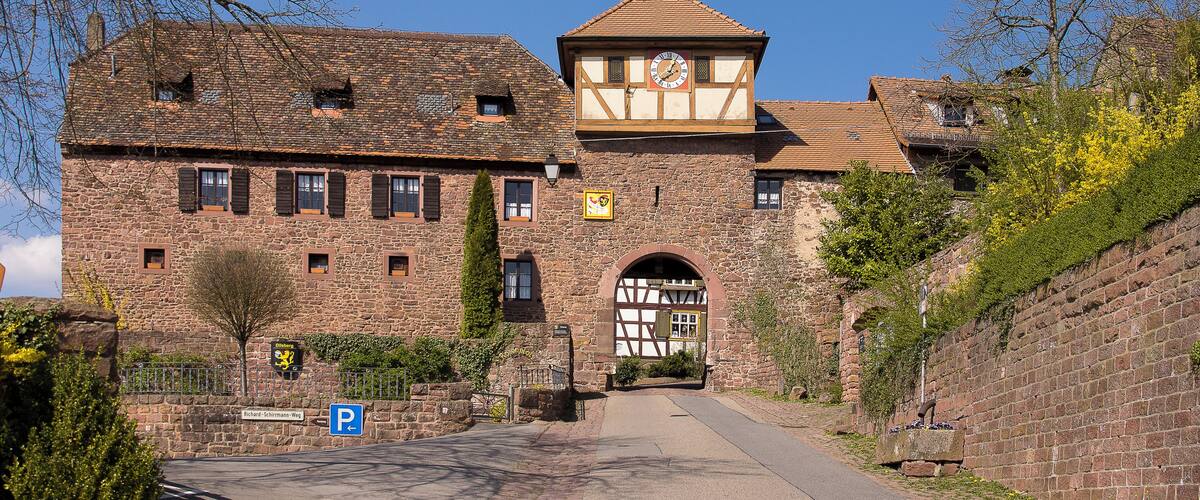 A historic stone building with a clock tower, a paved entrance, and a parking sign.