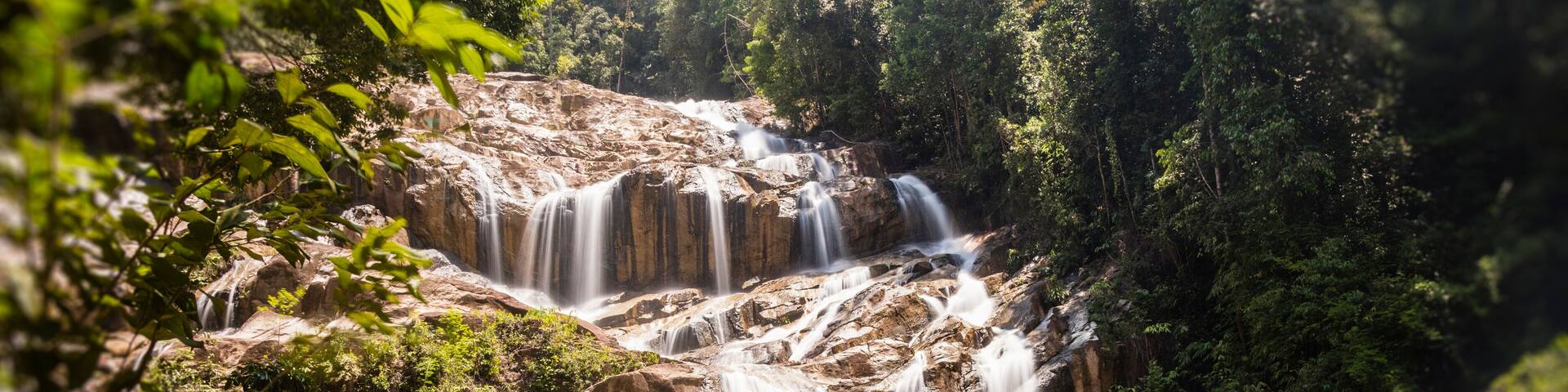 A multi-tiered waterfall surrounded by dense forest.