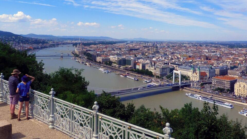 A cityscape with a river, a bridge, and a hill with people on a viewing platform.