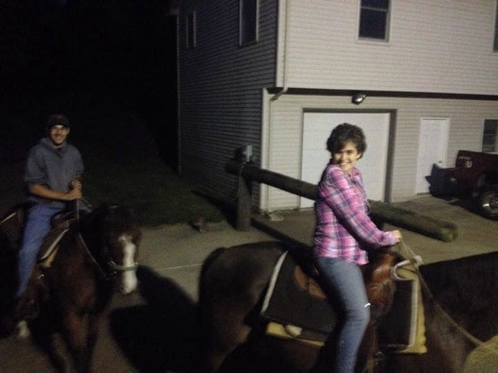 Two people riding horses in front of a house at night.