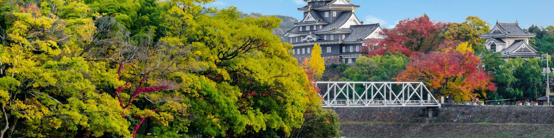 A traditional Japanese castle, a stone wall, and a bridge over a calm body of water.
