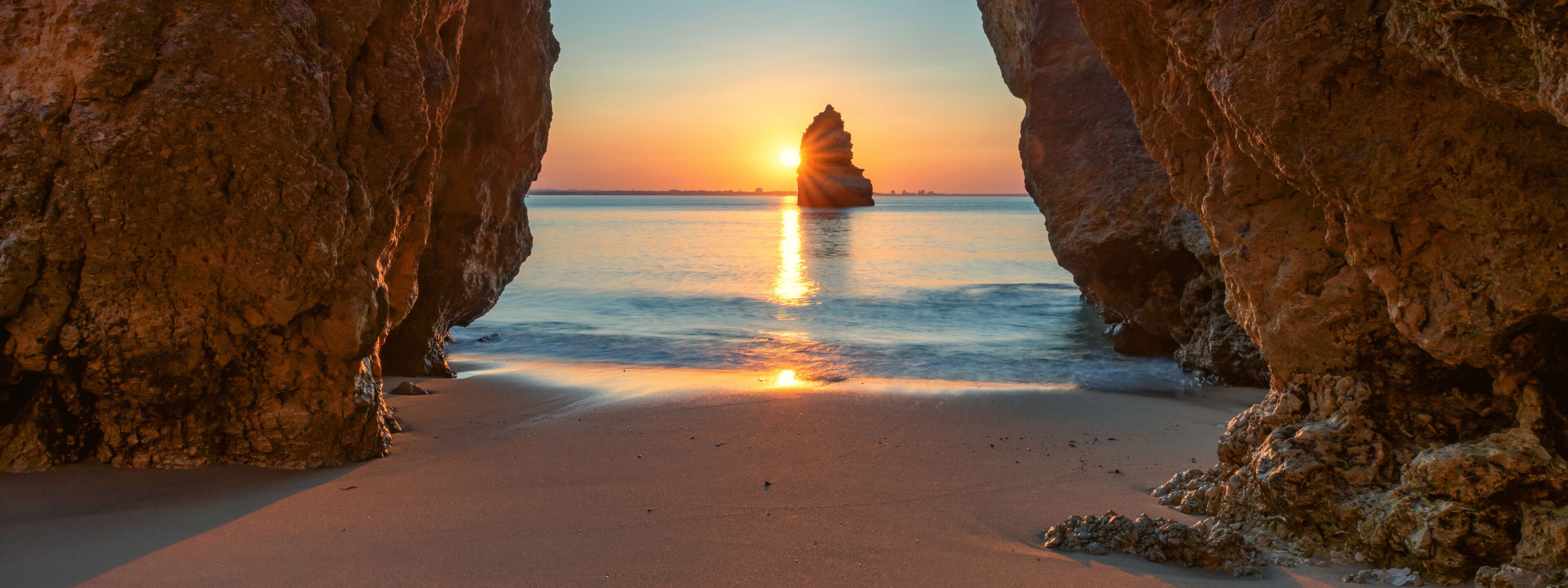 A sunset over a beach framed by rocky cliffs.
