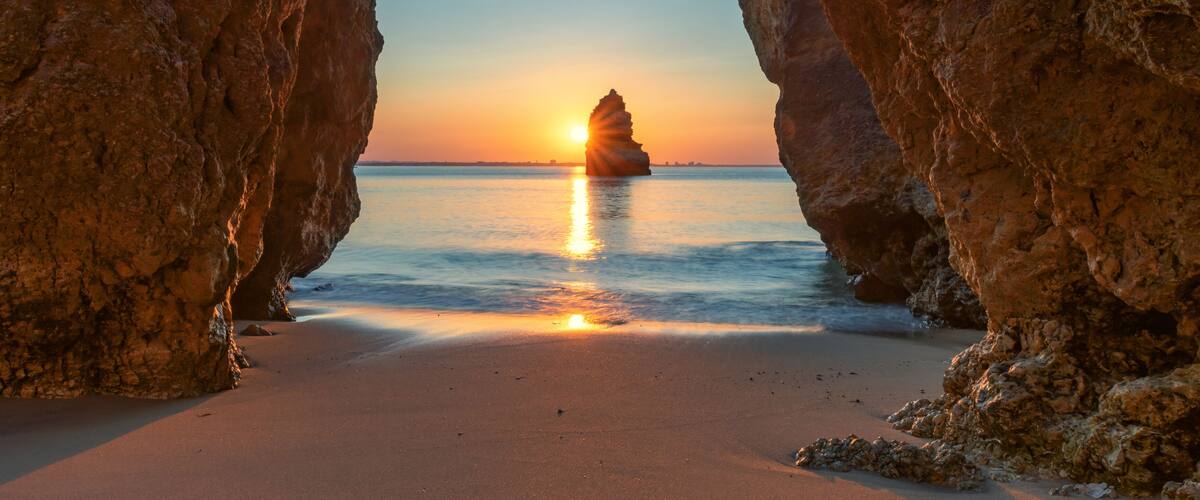 A sunset over a beach framed by rocky cliffs.