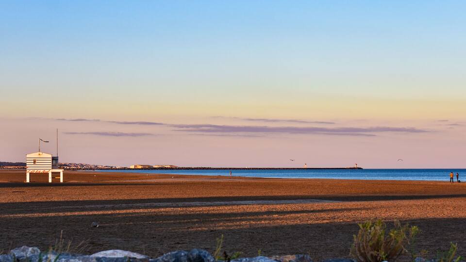 A beach with a lifeguard tower, rocky foreground, and a distant pier.