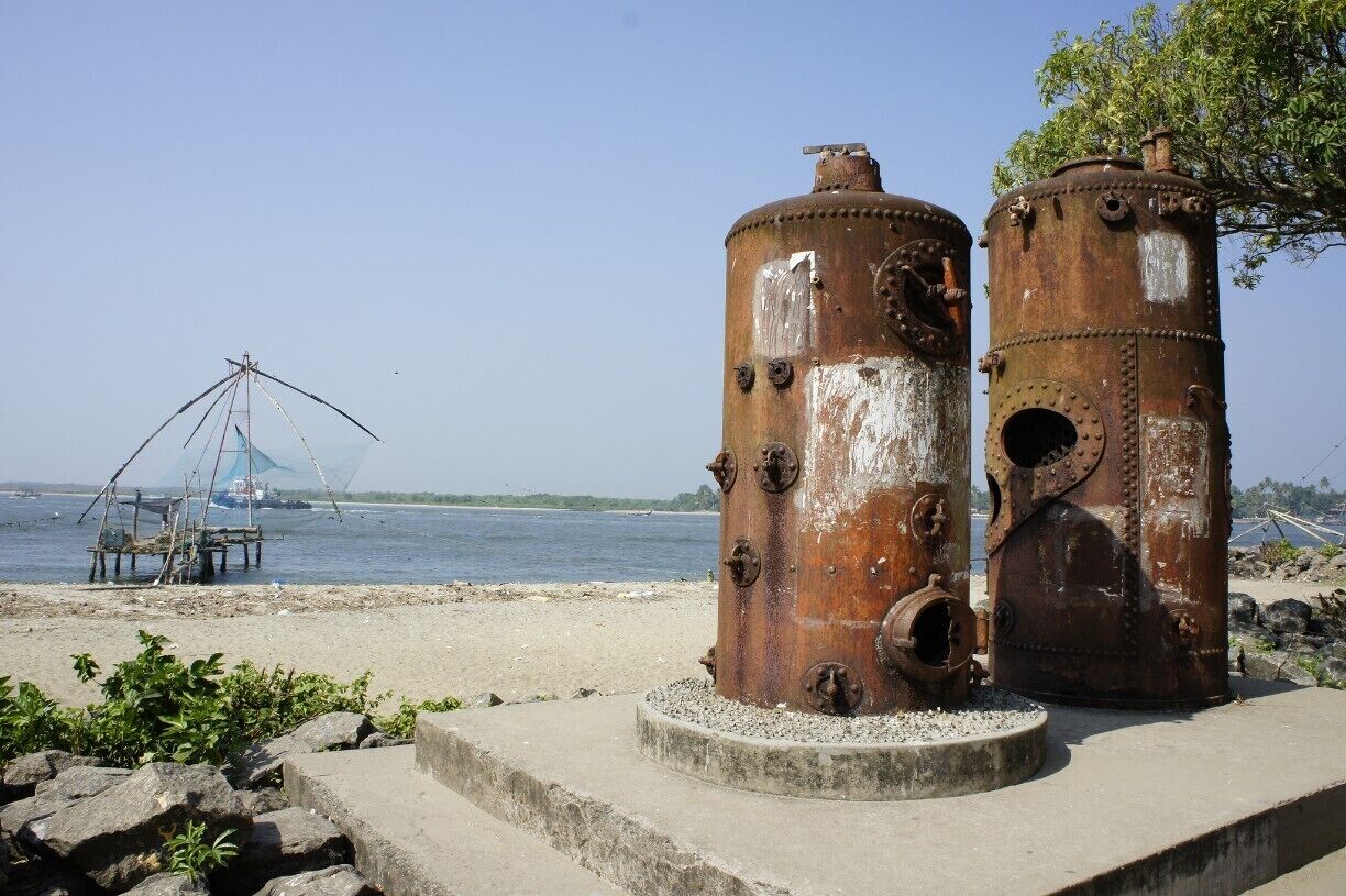 Dos estructuras metálicas cilíndricas y oxidadas sobre una plataforma de concreto junto a un cuerpo de agua, con una red de pesca al fondo.