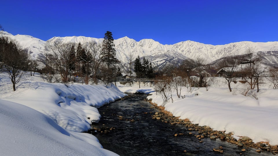 Un río cubierto de nieve que serpentea por un paisaje montañoso bajo un cielo azul despejado.