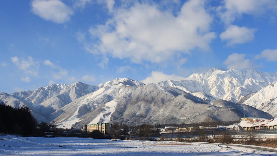 Cordillera nevada con cielo despejado y algunos edificios en primer plano.
