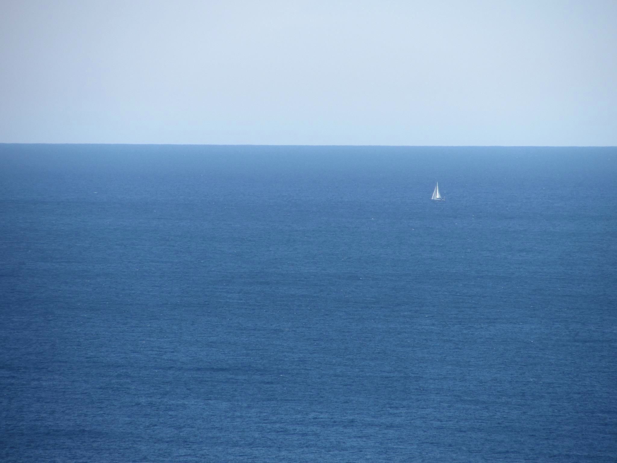 A calm sea with a small sailboat in the distance.