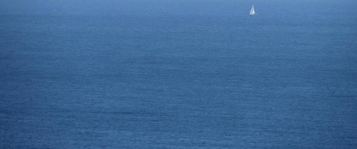 A calm sea with a small sailboat in the distance.