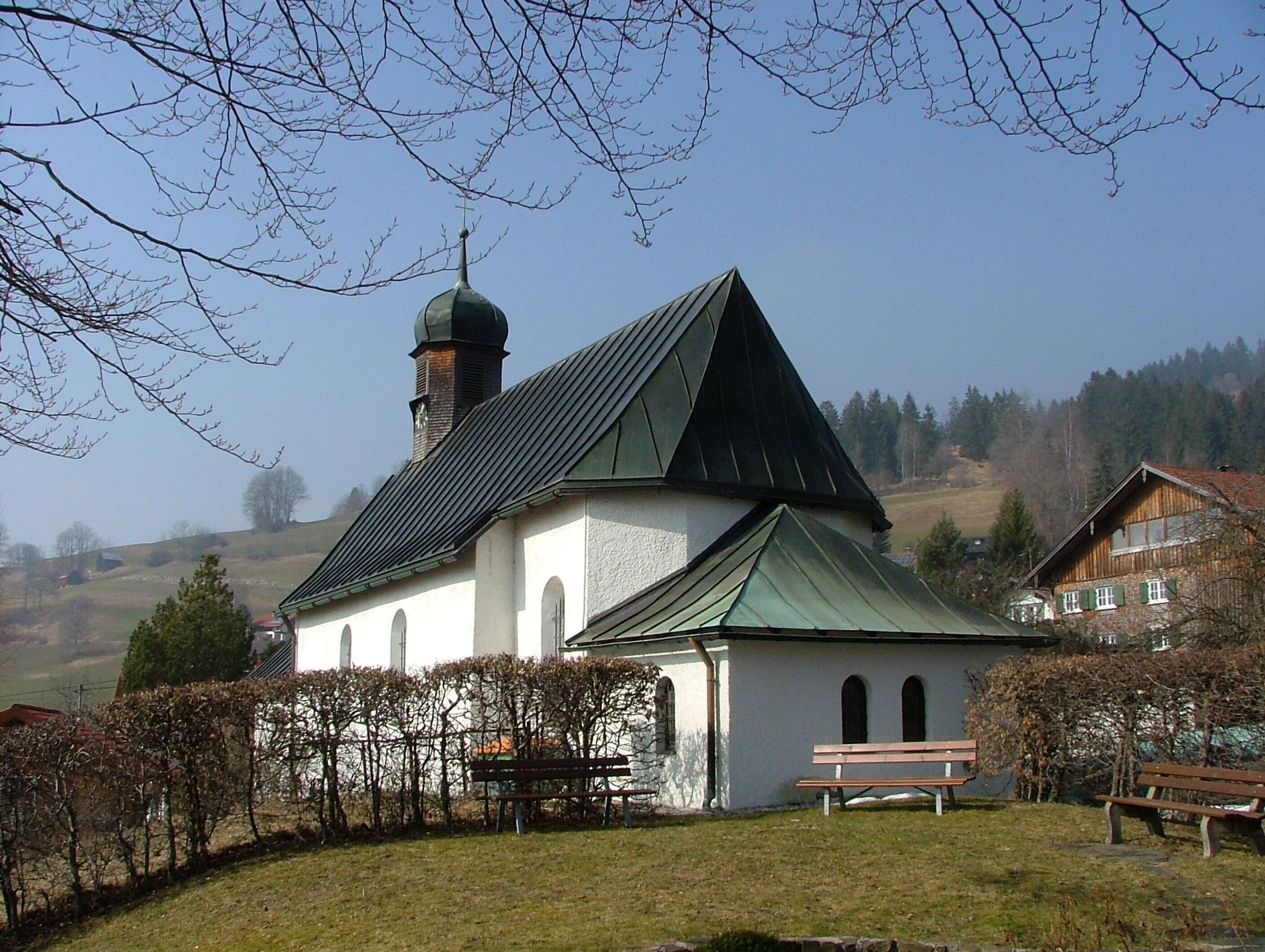 A church with a green roof and a bell tower, surrounded by a grassy area and benches.