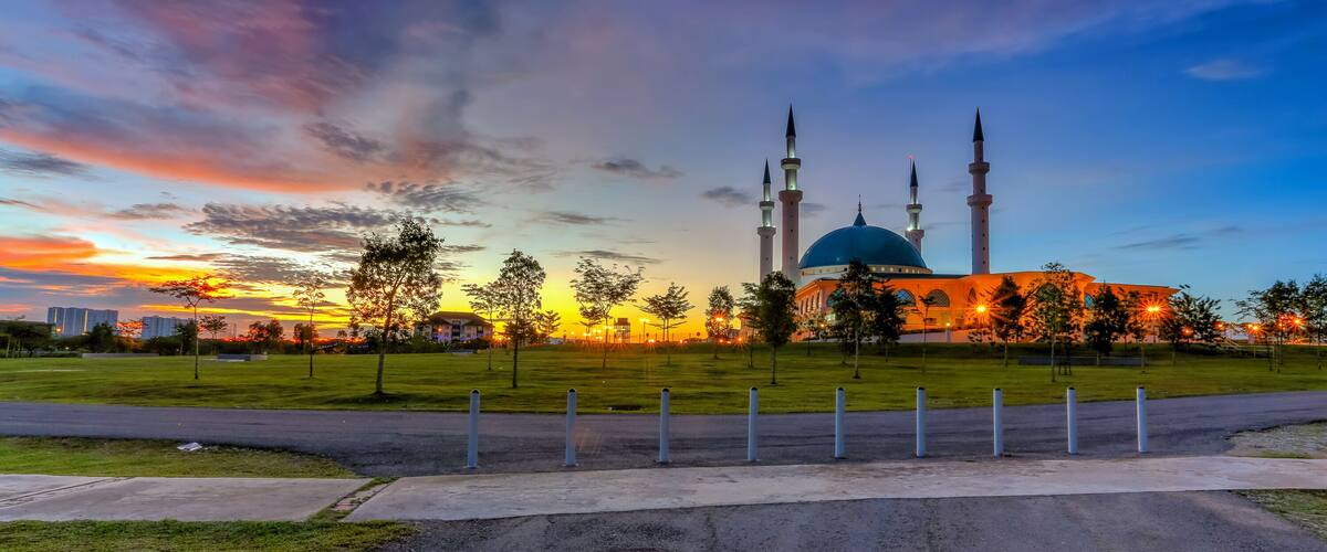 A mosque with a blue dome and three minarets, surrounded by a park with trees and a road.