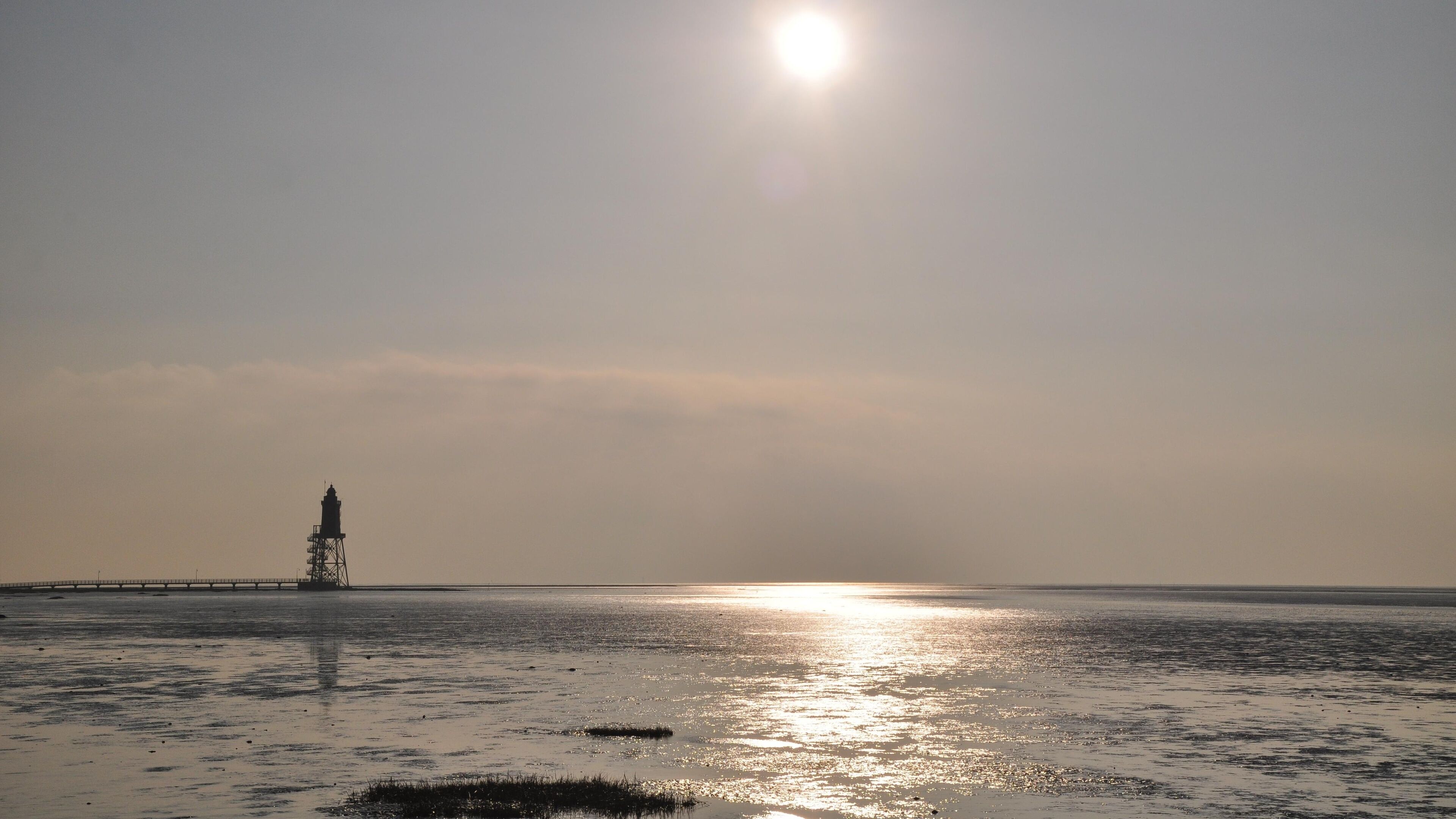 A lighthouse on a beach with the sun setting in the background.