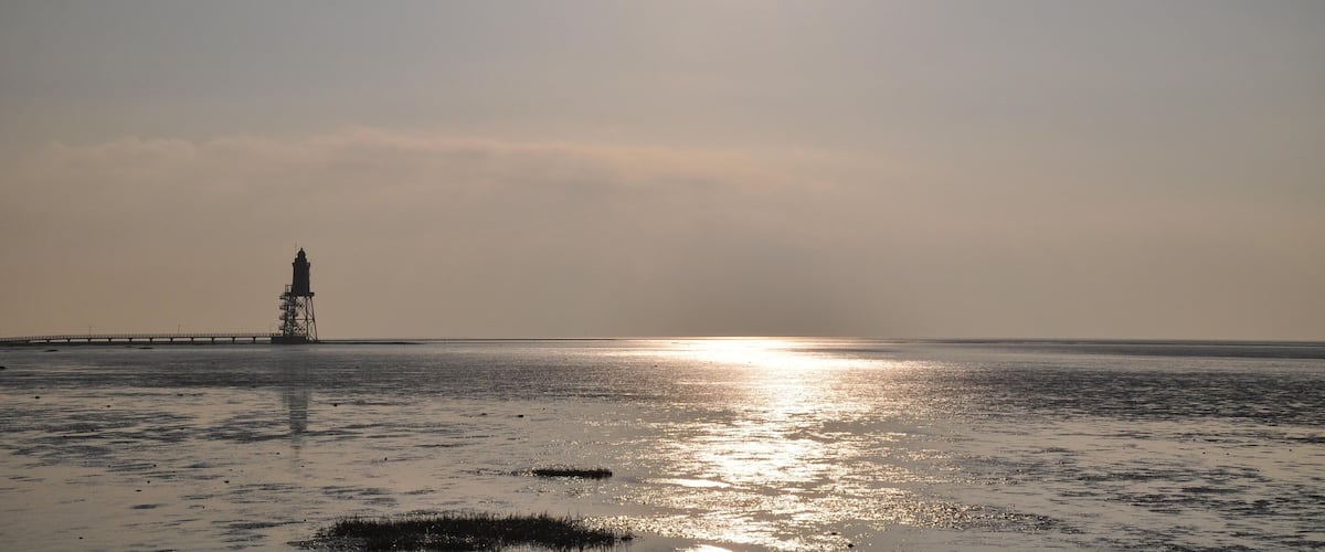 A lighthouse on a beach with the sun setting in the background.