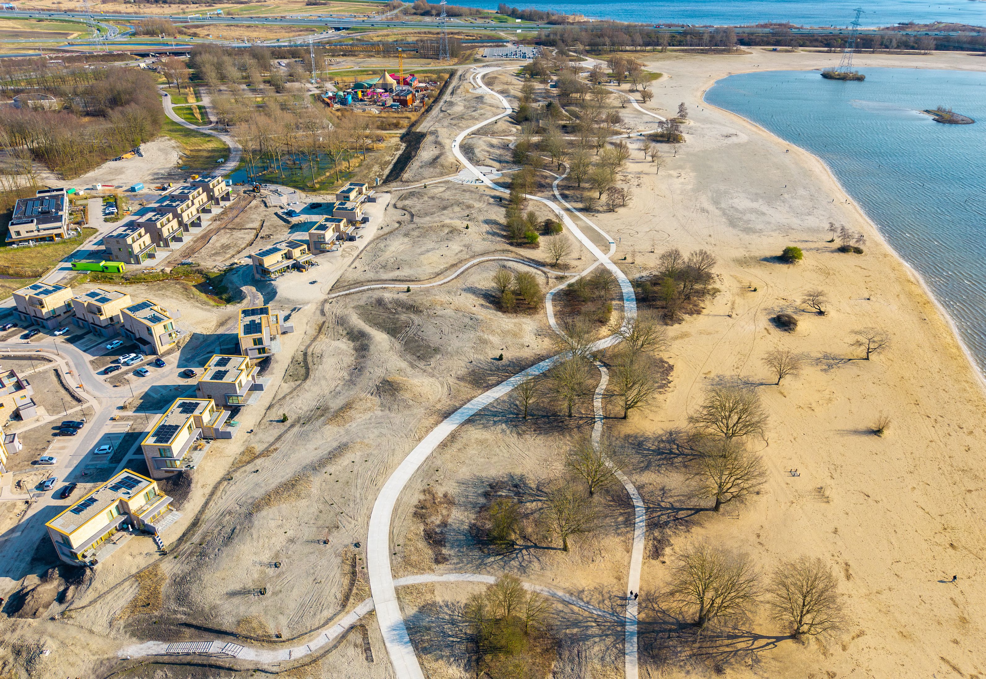 Eine Vogelperspektive zeigt eine Küstenlandschaft mit einer kurvenreichen Straße, Wohnhäusern und einem Strand.