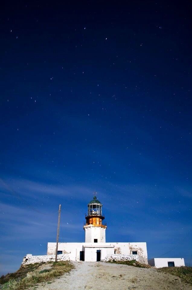A lighthouse with a white base and a yellow top, surrounded by a rocky landscape under a starry night sky.