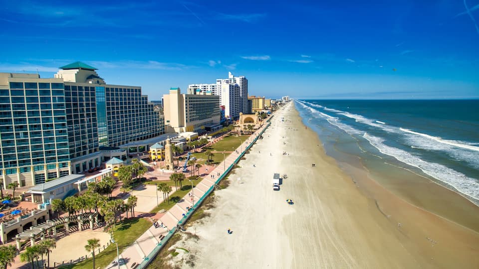 A coastal cityscape with a wide beach, high-rise buildings, and a clear blue sky.