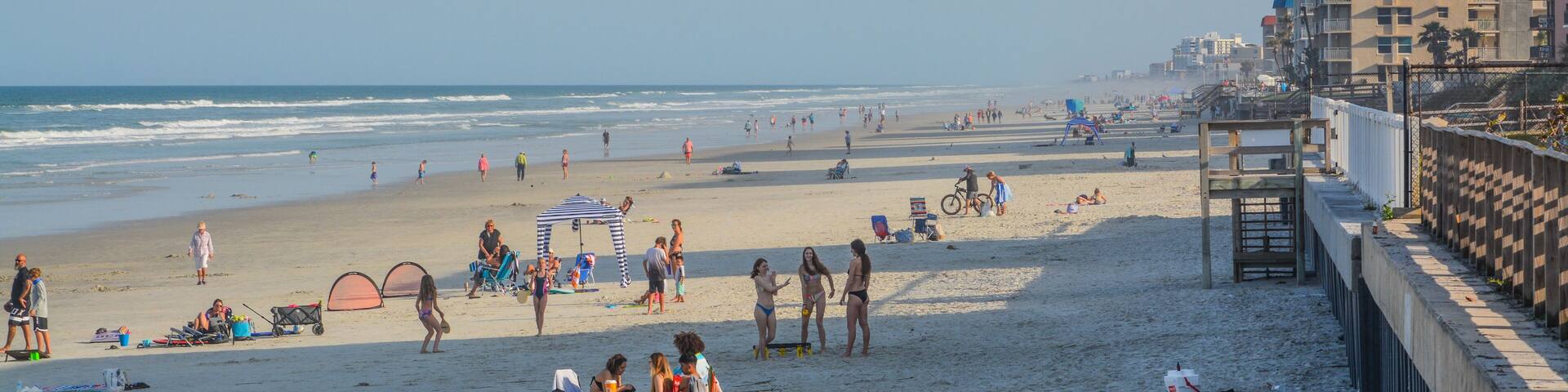 A crowded beach with people, tents, and a distant airplane.