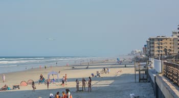 Una platja concorreguda amb persones, tendes i un avió a la distància.