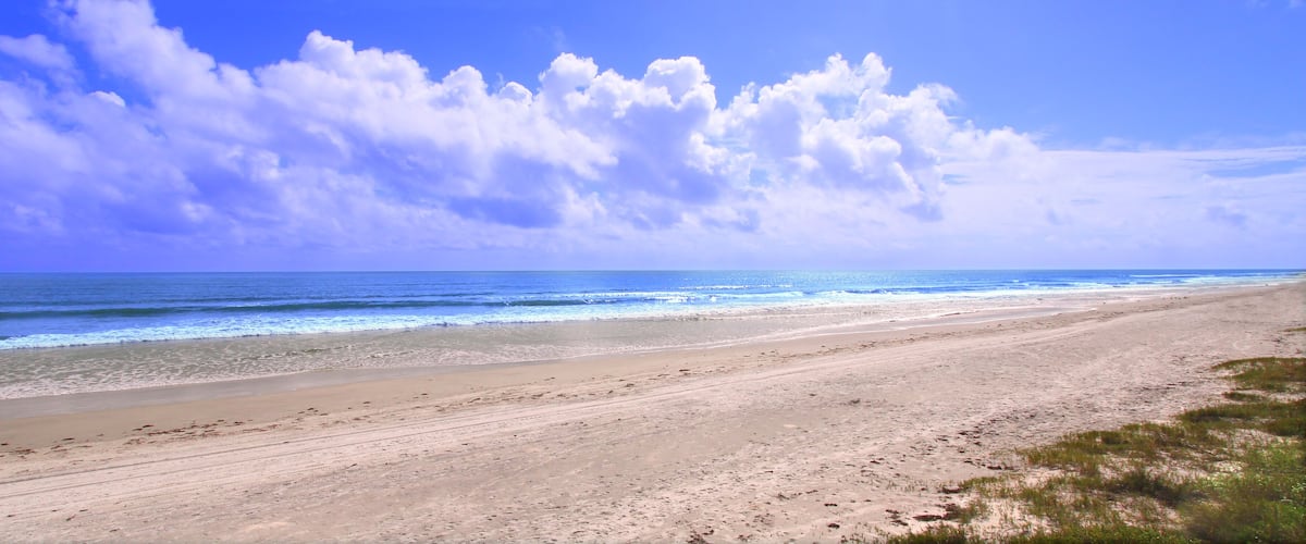 A beach with a sandy shore and ocean waves under a partly cloudy sky.