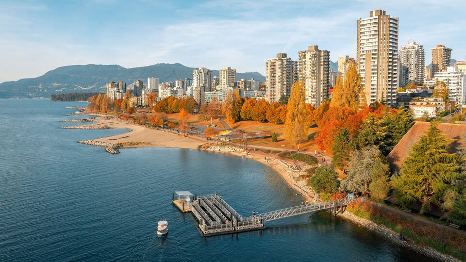 A waterfront cityscape with autumn foliage, a dock, and high-rise buildings.