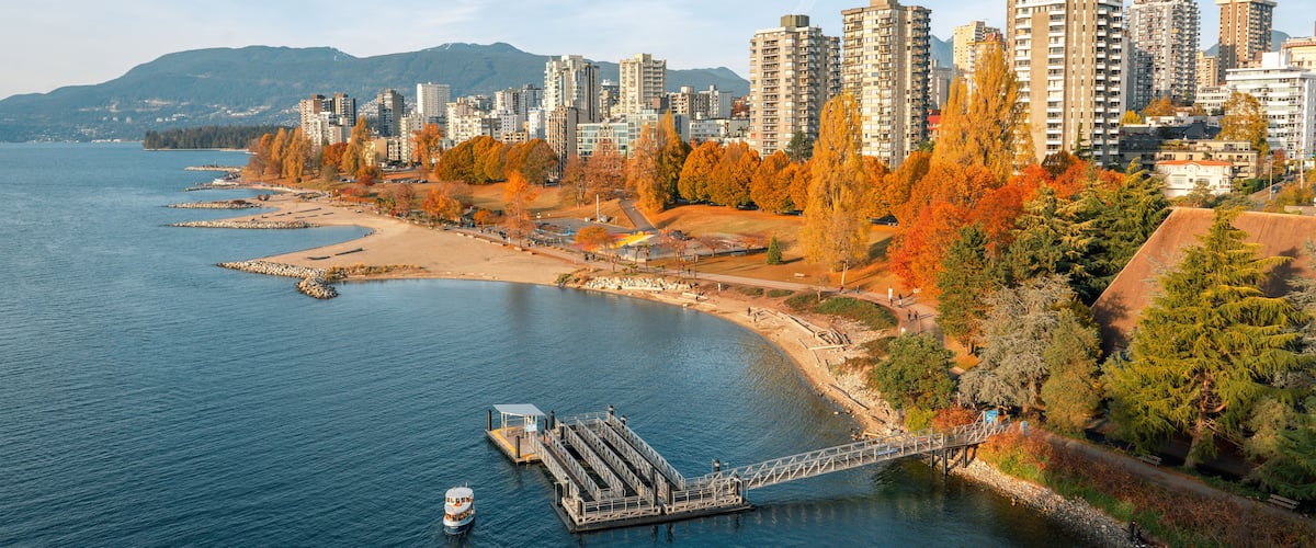 A waterfront cityscape with autumn foliage, a dock, and high-rise buildings.
