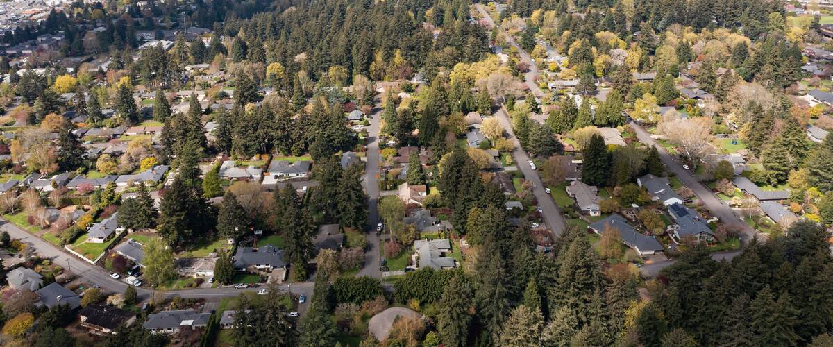 Aerial drone view of Southwest Portland, Oregon, featuring residential neighborhoods, tree-lined streets, rolling hills, and urban landscape with the downtown skyline visible in the distance