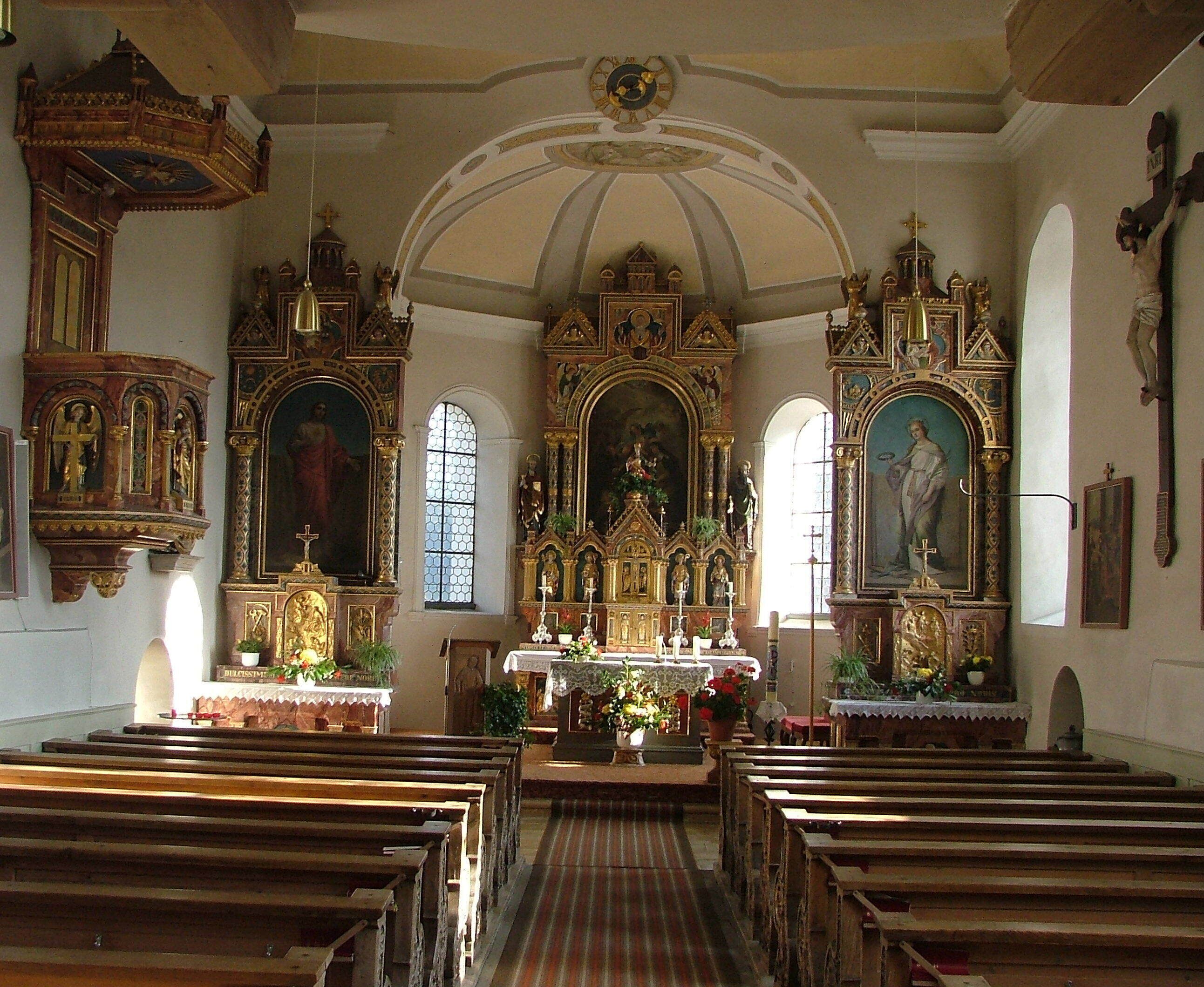 An ornate church interior with wooden pews, a central altar, and religious paintings.